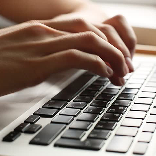 A hand is posed over a computer keyboard, typing