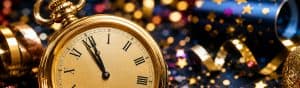 Close-up of a gold clock showing almost midnight, surrounded by New Year party decorations like confetti and streamers, symbolizing celebration and new beginnings.