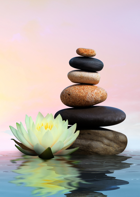 Varied colored stacked stones rise from calm water, with a water lilly floating beside the stack.
