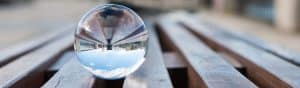A clear glass sphere reflecting a cityscape, placed on wooden benches, symbolizing clarity and focus in leadership and encouraging others.