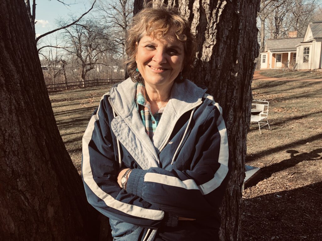 Lynn Sanders, Story Empowerment Coach, leaning up against a tree, loving nature.