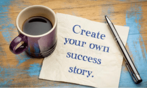 A cup of coffee sits on a note that is on a desktop with a pen nearby. The message on the note says, "Create your own success story."