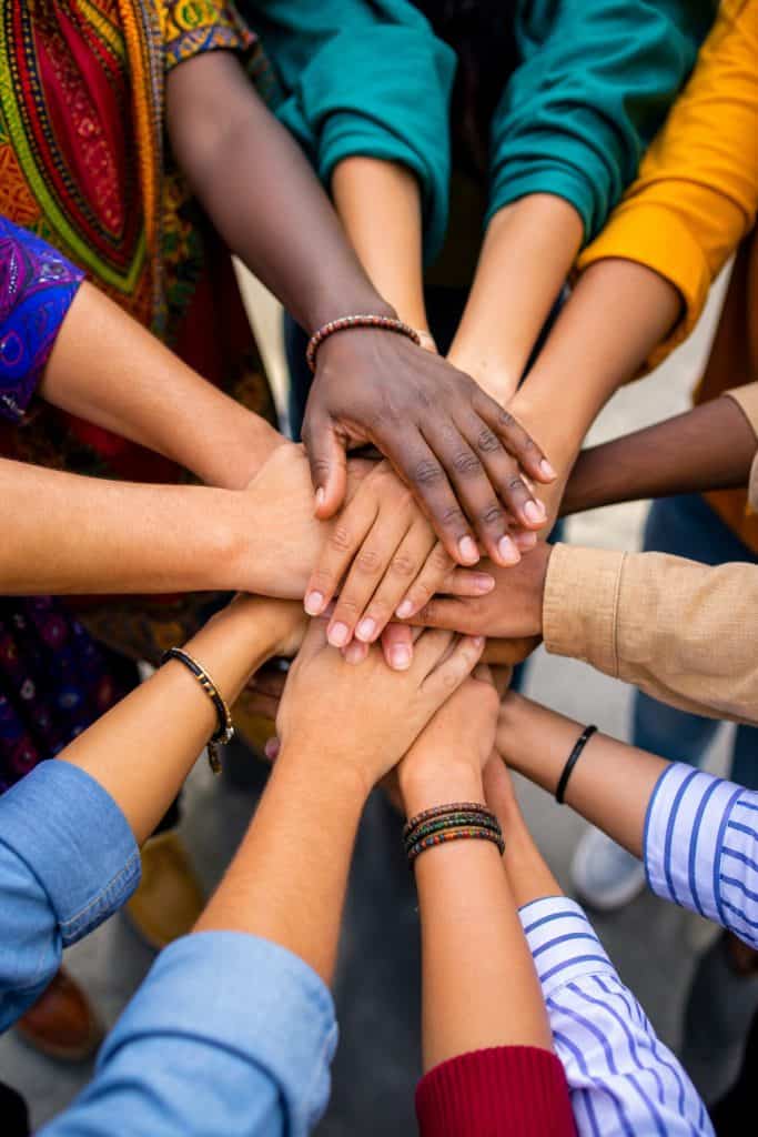 Diverse group of people placing their hands together in a symbol of teamwork, collaboration, and shared values, emphasizing the importance of unity and collective effort.
