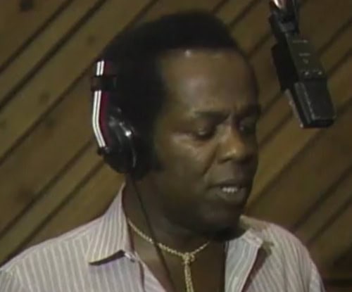 Experienced professional recording in a studio setting, wearing headphones and focused on the audio work.