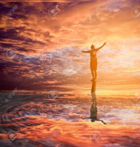 Person standing on a rock with arms outstretched at sunset, symbolizing confidence and self-discovery.