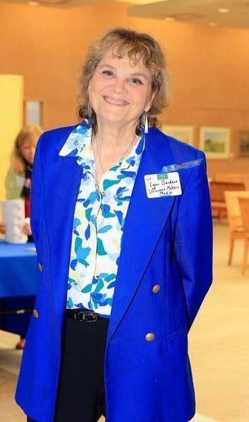 Experienced woman speaker at a professional event, smiling confidently in a blue blazer and patterned blouse, promoting leadership and empowerment.